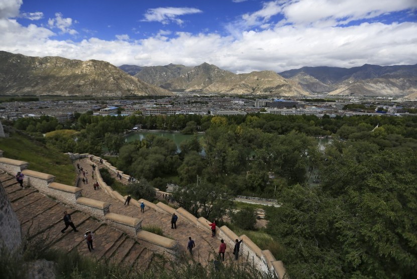 Turis menaiki anak tangga di Istana Potala dengan pemandangan Kota Lhasa, Tibet.