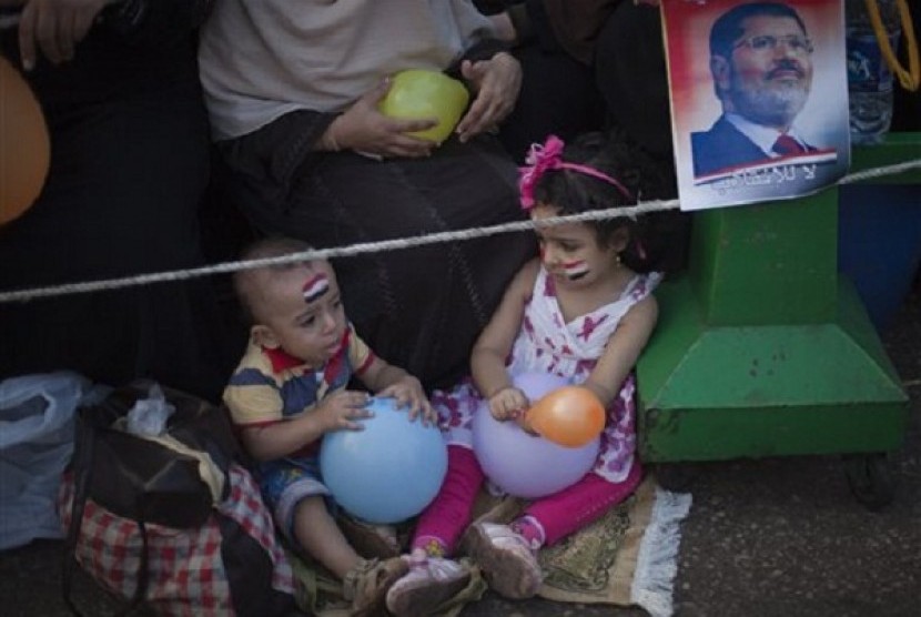 Two Egyptian children play with balloons as they sit next to a picture of Mursi outside Rabaah al-Adawiya mosque, where supporter of Egypt's ousted President Mohammed Mursi have installed a camp and held daily rallies at Nasr City, Cairo, Egypt, Tuesday, A