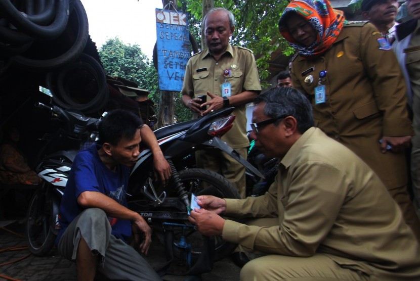 Wakil Walikota Tangerang Selatan Benyamin Davnie (jongkok kanan) memeriksa kartu identitas warga yang berprofesi penambal ban di Serpong, Tangerang Selatan, Banten, Selasa (19/7). 