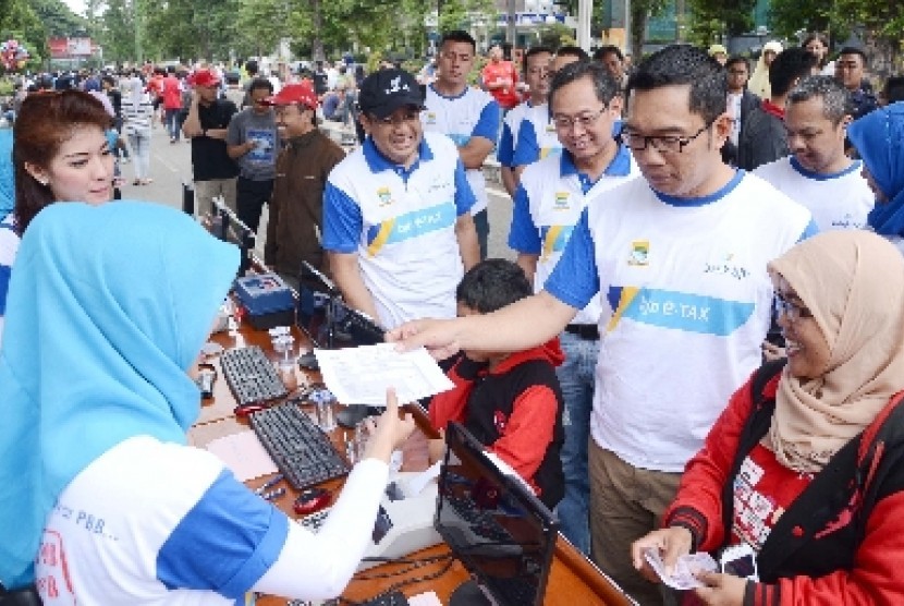 Wali Kota Bandung Ridwan Kamil (kanan) dan Dirut Bank BJB Bien Subiantoro (bertopi) bersama para pembayar PBB pada launching 'PBB Online Mobile'di Kota Bandung, Ahad (23/2).