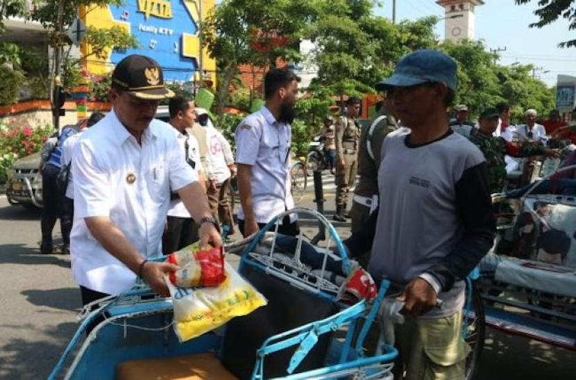 Wali Kota Madiun, Maidi, membagikan bantuan paket bahan pokok untuk tukang becak di jalan depan Balai Kota Madiun, Jawa Timur, Rabu (3/4/2024). 