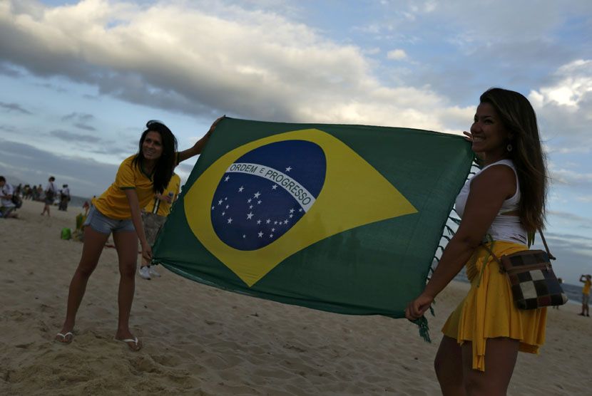 Wanita Brasil membentangkan bendera negaranya sebelum Timnas Brasil menghadapi Kroasia di laga Grup A Piala Dunia 2014 di pantai Copacabana, Rio de Janeiro, Kamis (12/6). 