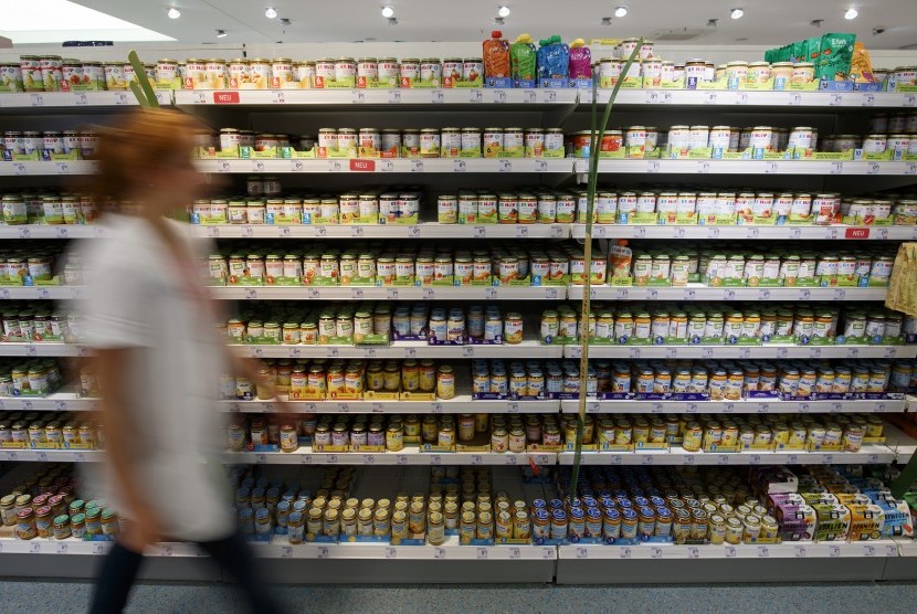 Wanita melintasi rak makanan bayi di sebuah supermarket.