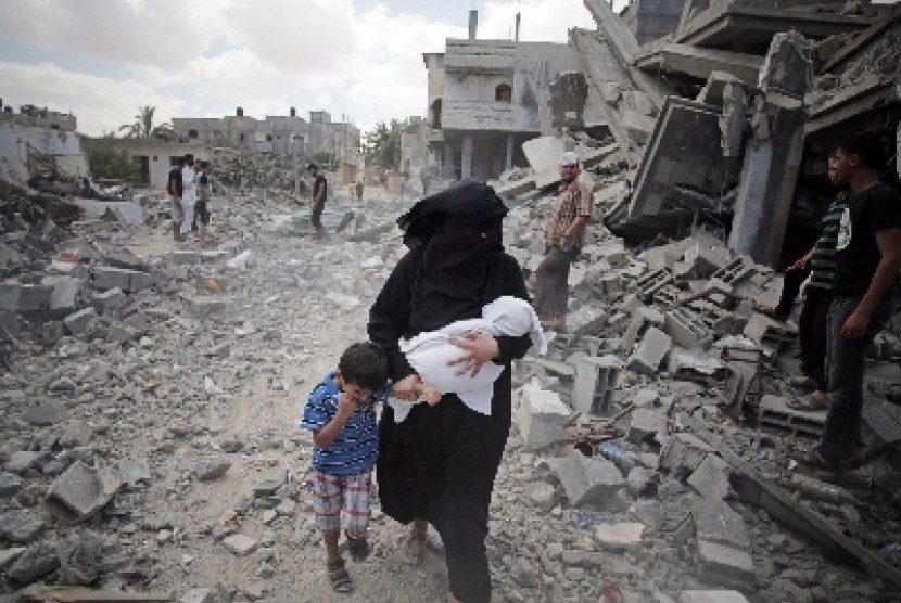 Wanita Palestina menggendong anaknya melewati reruntuhan bangunan yang hancur akibat rudal Israel.