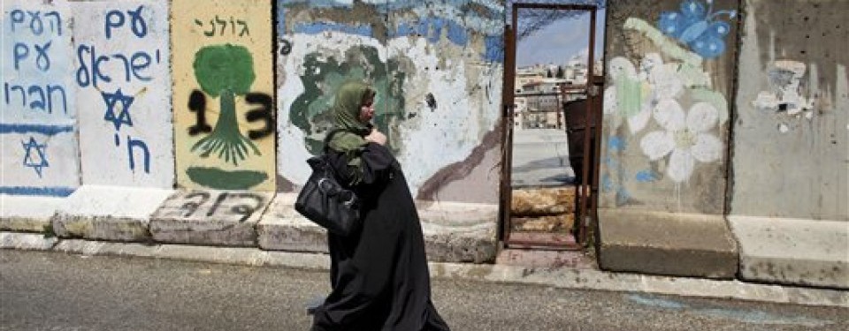     Wanita Palestina tengah berjalan di depan tembok beton yang memblokade kota Hebron, Tepi Barat. 