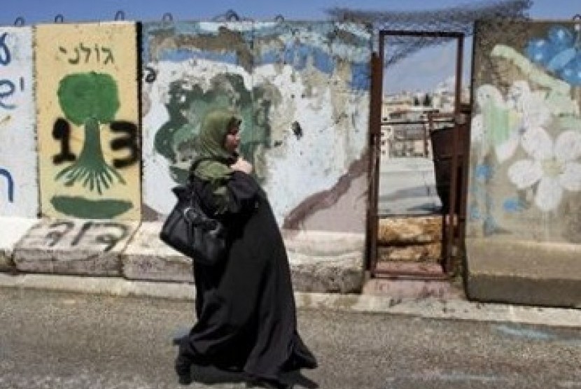     Wanita Palestina tengah berjalan di depan tembok beton yang memblokade kota Hebron, Tepi Barat. 