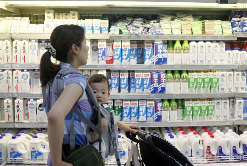 Seorang ibu menggendong bayinya berjalan melewati rak susu sapi di supermarket. Protein A1-beta-casein dalam susu sapi disebut dapat menyebabkan masalah kesehatan tertentu.