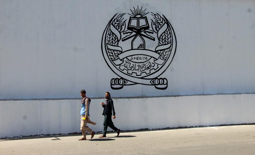 Warga Afghanistan melewati gedung bekas kedutaan AS saat dinding yang dicat dengan segel pemerintah Taliban Emirat Islam Afghanistan di Kabul, Afghanistan, 08 September 2021.