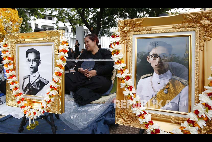 Warga Bangkok di antara dua foto raja saat  mengikuti prosesi kremasi dan penguburan jenazah mendiang Raja Bhumibol Adulyadej di Bangkok.