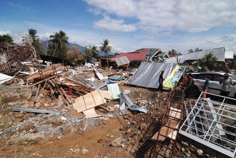 Warga berada di dekat rumah dan bangunan yang luluh lantak akibat gempa di Desa Lolu, Sigi, Sulawesi Tengah, Senin (8/10).