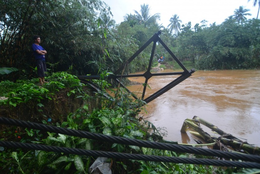 Warga berada di dekat sisa tiang jembatan gantung yang ambruk terbawa arus sungai Cibeurem, Desa Pajaten, Kabupaten Pangandaran, Jawa Barat, Sabtu (7/10). Hujan deras yang mengguyur wilayah Pangandaran mengakibatkan air sungai Cibeurem meluap serta mengikis jembatan.