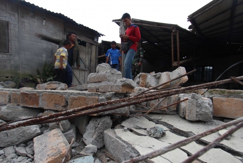 Warga berada di rumah yang runtuh akibat gempa di Desa Kabayaken Kecamatan Namanteran, Kabupaten Karo, Sumatera Utara, Senin (17/1).