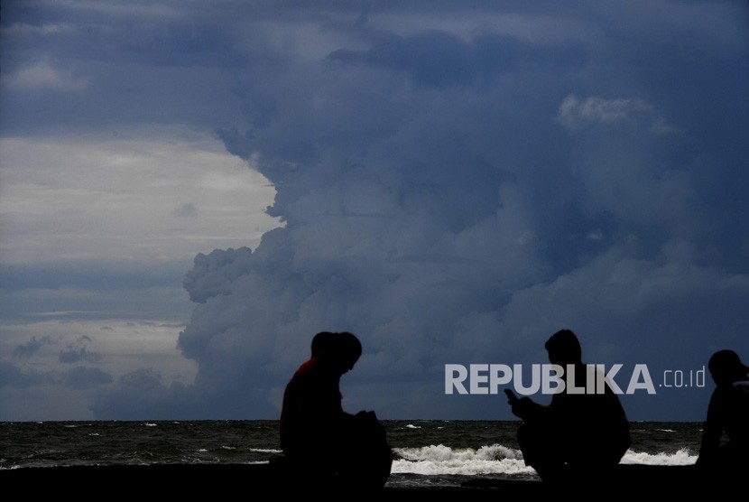 Warga beraktivitas dengan latar belakang awan panas semburan Gunung Anak Krakatau terlihat dari kawasan Carita, Pandeglang, Banten, Jumat (28/12/2018). 