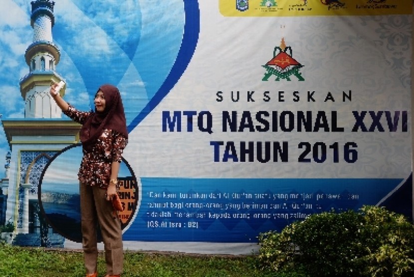 Warga berfoto di depan spanduk MTQ Nasional yang menghiasi jalanan di Kota Mataram, NTB, Kamis (14/7).