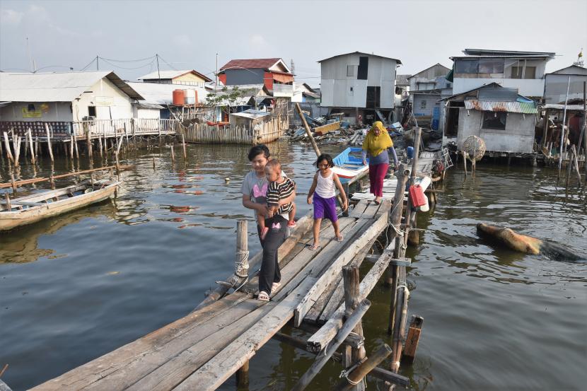 Warga berjalan di atas jembatan kayu di perkampungan nelayan Muara Angke, Jakarta Utara. Berdasarkan hasil proyeksi, pada 2050 kenaikan muka air laut akan membanjiri daerah Jakarta seluas lebih kurang 160,4 kilometer persegi atau 24,3 persen dari luas total Jakarta. 