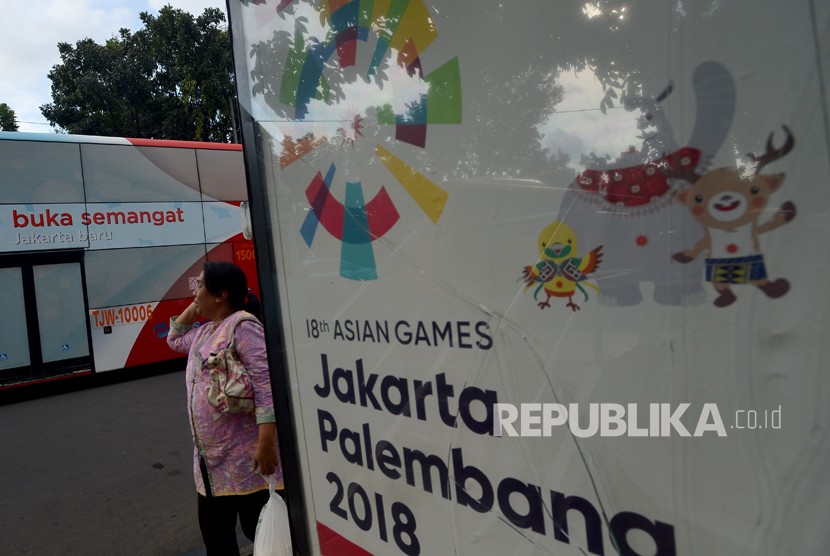 Warga berjalan di samping papan promosi Asian Games XVIII di Kawasan Jalan Merdeka Selatan, Jakarta, Jumat (20/4).