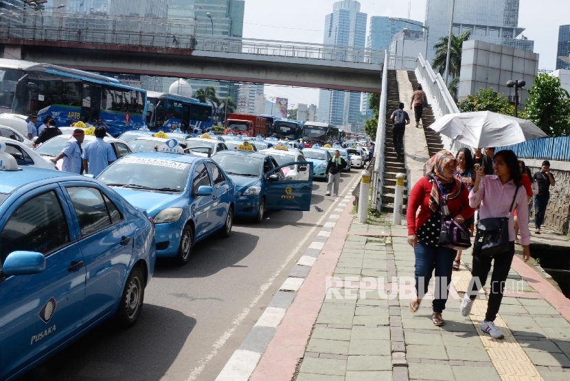 Warga berjalan kaki saat Ribuan sopir taksi dan angkutan umum lain melakukan aksi di Jakarta, Selasa (22/3).