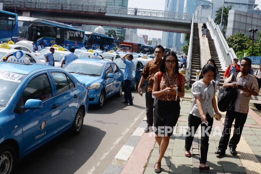 Warga berjalan kaki saat ribuan sopir taksi dan angkutan umum lain melakukan aksi di Jakarta, Selasa (22/3). (Republika/Yasin Habibi)