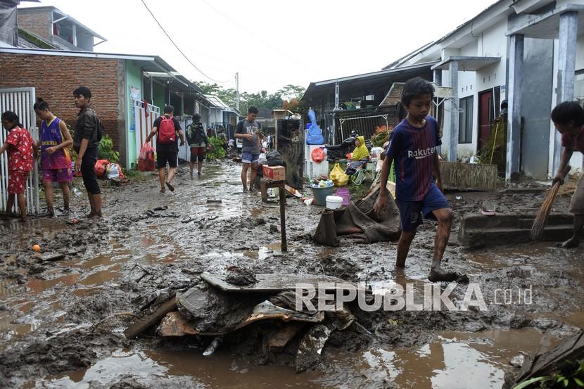 Warga berjalan melewati endapan lumpur pascabanjir di salah satu perumahan di Kelurahan Tegal Besar, Kaliwates, Jember, Jawa Timur.