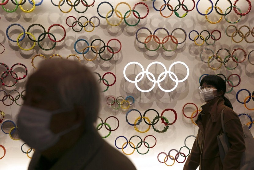 Warga bermasker melintasi Museum Olimpiade di Tokyo, Jepang. Olimpiade 2020 Tokyo ini ditunda sampai 2021 yang merupakan pertama kalinya sebuah olimpiade ditunda dalam 124 tahun sejarah olimpiade.