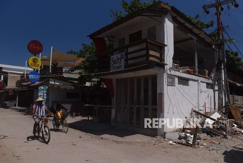 Warga bersepada di samping bangunan yang rusak akibat gempa bumi di Gili Trawangan, Lombok Utara, NTB, Kamis (9/8).