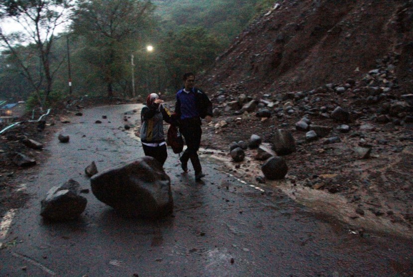 Warga berusaha melintasi material longsor yang jatuh di ruas jalan nasional Trenggalek-Ponorogo Kilometer 16, Trenggalek, Jawa Timur, Rabu (25/1).