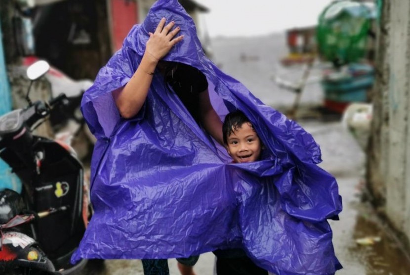 Warga di Cavite City, Filipina berjalan menggunakan mantel. Sebanyak 200 ribu orang di Filipina dievakuasi akibat topan Kammuri pada Selasa (3/12).