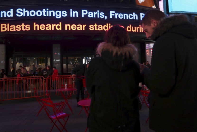 Warga di Manhattan, AS, memperhatikan berita lewat running text mengenai penembakan yang terjadi di Paris, Prancis, Jumat malam waktu setempat (13/11).