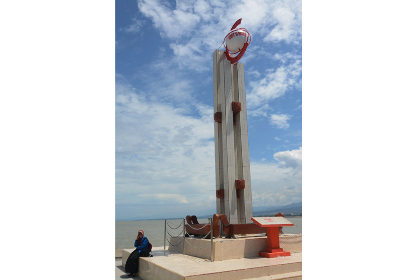 Warga duduk di dekat monumen Gerhana Matahari Total yang dibangun di bibir pantai Teluk Palu, Sulawesi Tengah, Selasa (8/3).