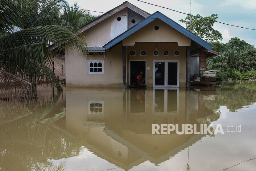 Warga duduk di depan pintu rumahnya yang terendam banjir luapan Sungai Kampar (ilustrasi). 