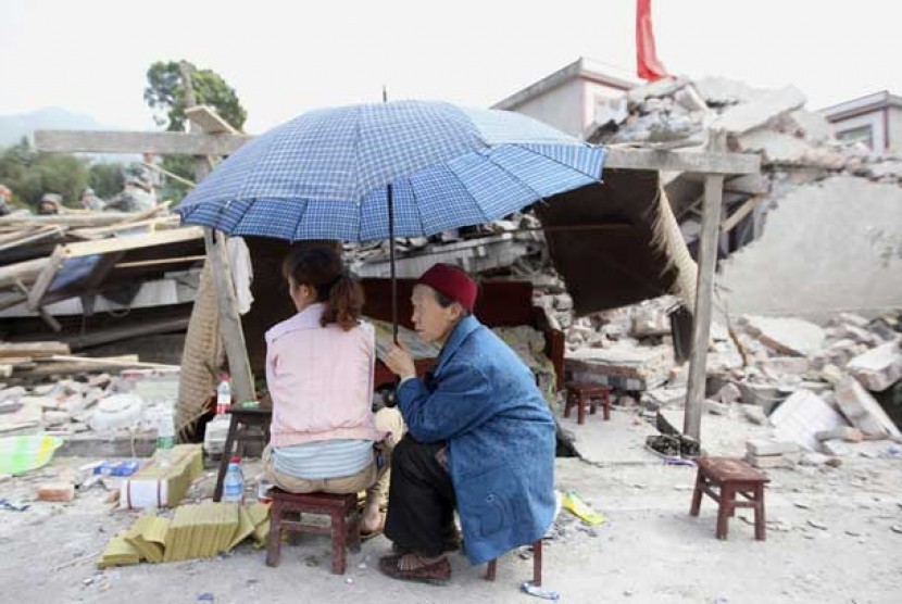  Warga duduk di samping reruntuhan rumah yang hancur akibat gempa bumi di Longmen Township, Lushan County, Ya'an, provinsi Sichuan,Cina, Sabtu (20/4).