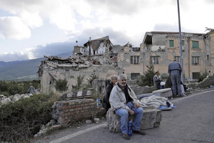 Warga Italia duduk di tepi jalan. Gedung yang hancur di Amatrice, Italia terlihat di belakangnya, Rabu, 24 Agustus 2016.