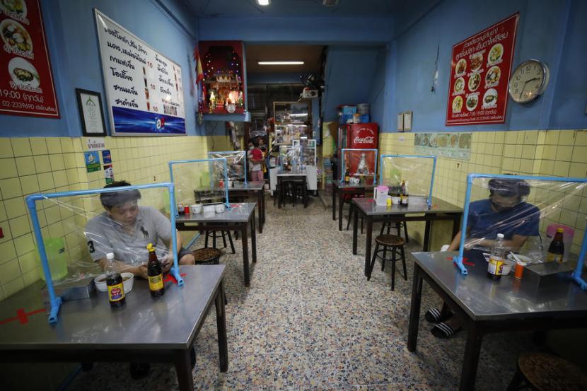 Warga makan di balik pemisah dari plastik di sebuah kedai di Bangkok, Thailand, Rabu (13/5). WHO mengingatkan masyarakat mungkin akan harus hidup penuh kewaspadaan dalam waktu lama akibat virus corona.