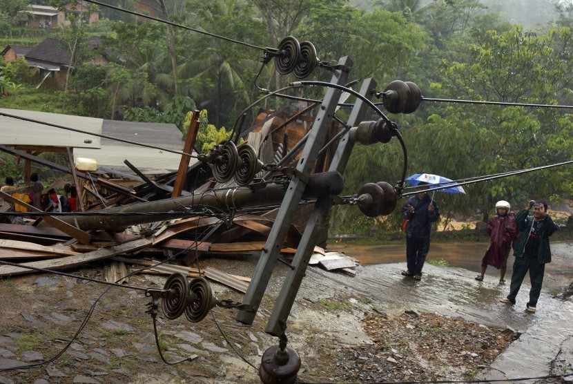 Warga melintas dekat tiang listrik yang roboh menimpa rumah penduduk akibat longsor (ilustrasi) 