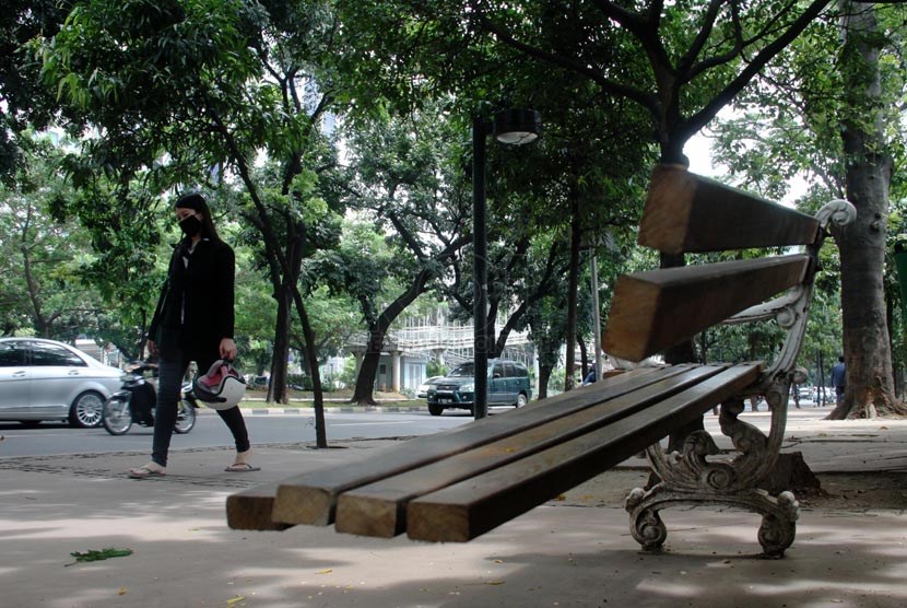 Warga melintas di bangku taman yang rusak di Jalan Sudirman, Jakarta Pusat, Kamis (10/4).