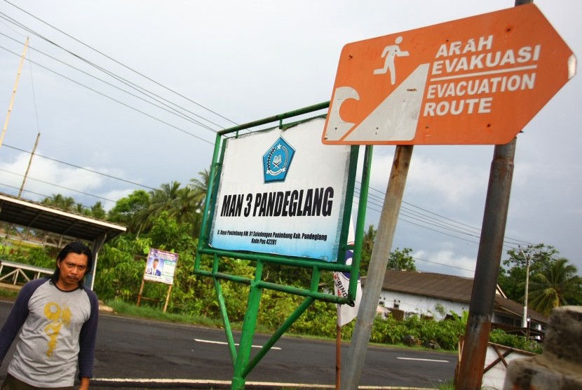 Warga melintas di bawah papan petunjuk arah evakuasi bencana tsunami yang ada di kawasan Panimbang, Pandeglang, Banten, Selasa (25/12/2018).