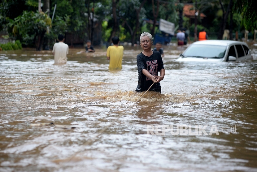  Warga melintas di dekat mobil yang terendam air luapan Sungai Ciliwung, Bukit Duri, Jakarta, Kamis (16/2). 