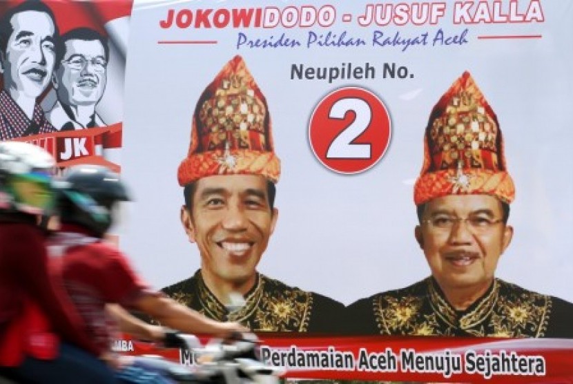 Warga melintas di depan alat peraga kampanye (APK) pasangan capres cawapres Jokowi - Jusuf Kalla yang memakai pakaian adat Aceh di Kota Lhokseumawe, Aceh, Senin (23/6). 