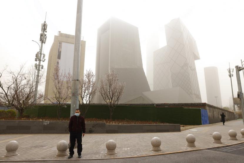 Warga melintas di depan gedung pencakar langit di Beijing di tengah badai pasir, Ahad (28/3).