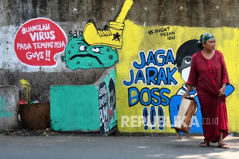 Warga melintas di depan mural berisi ajakan menjaga jarak di Jalan Pahlawan Komarudin RW 03, Cakung Barat, Jakarta Timur. Pada Rabu (25/11) kasus Covid-19 bertambah 5.534 kasus baru.