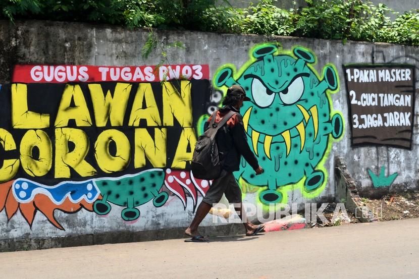Warga melintas di depan mural berisi ajakan menjaga jarak di Jalan Pahlawan Komarudin RW 03, Cakung Barat, Jakarta Timur. Protokol kesehatan tetap harus dilakukan meski vaksin sudah tersedia. 