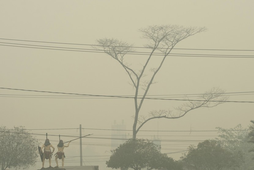 Warga melintas di depan patung orang dayak yang masih diselimuti asap di Palangkaraya, Kalimantan Tengah, Kamis (1/10).