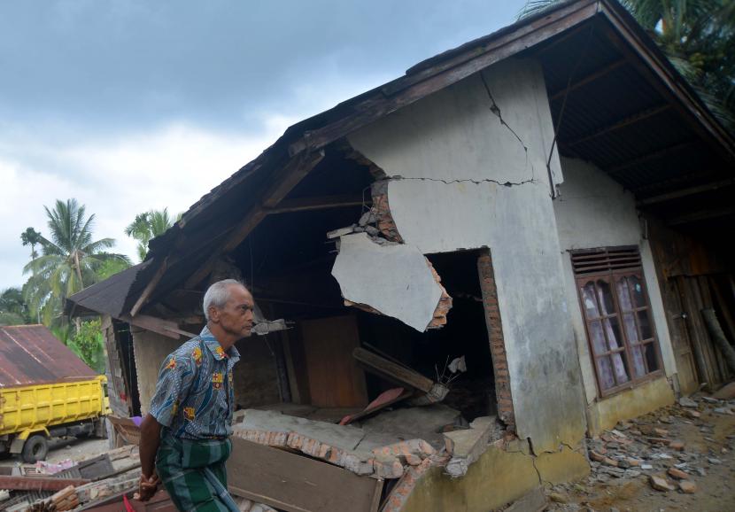 Warga melintas di depan rumah yang rusak akibat gempa (ilustrasi)