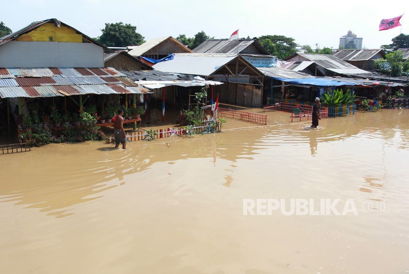Warga melintas di depan tempat tinggalnya yang terendam banjir akibat meluapnya sungai Cisadane di kawasan Karawaci, Tangerang, Banten, Jumat (26/4/2019). 