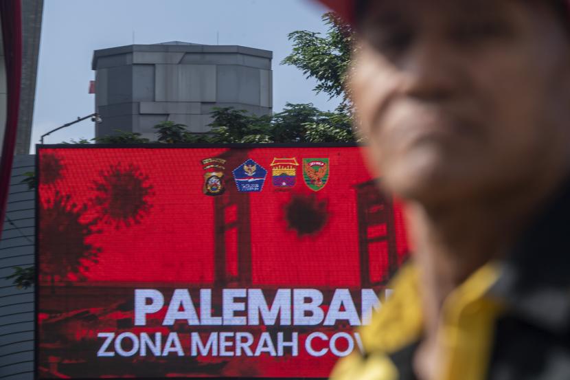 Warga melintas di Jalan Jenderal Sudriman dengan latar videotron bertuliskan Palembang zona merah COVID-19 di Palembang, Sumatera Selatan