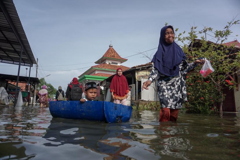 Warga melintas di jalan yang tergenang banjir di Pekalongan. 