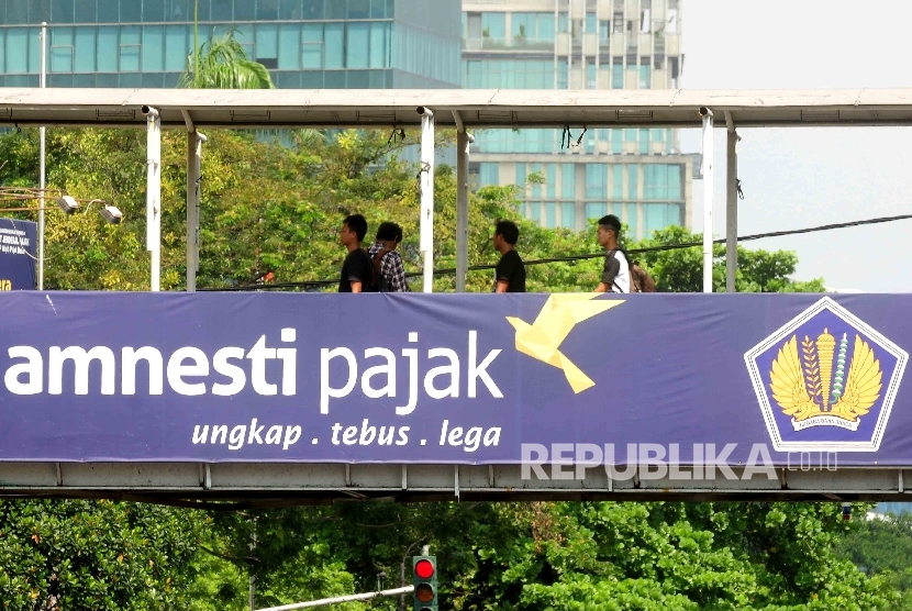 Warga melintas di jembatan penyebrangan orang (JPO) yang terpasang spanduk sosialisai pengampunan pajak di kawasan Stasiun Gambir, Jakara, Ahad (31/7).  (Republika/ Agung Supriyanto)