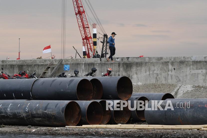 Warga melintas di samping alat yang digunakan untuk pembangunan tanggul pengaman laut atau National Capital Integrated Coastal Development (NCICD) di Kawasan Muara Baru Jakarta, Senin (10/1/2022). Pemprov DKI Jakarta yang berkolaborasi dengan Kementerian PUPR dan Pemprov Jawa Barat telah menyelesaikan pembangunan tanggul laut sepanjang 12,6 kilometer dari target prioritas sepanjang 46 kilometer untuk mengantisipasi banjir rob di pesisir utara ibu kota. 