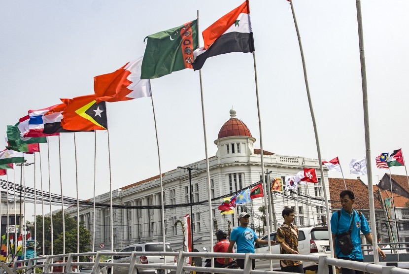 Warga melintas di samping deretan bendera negara peserta Asian Games 2018 yang dipasang di kawasan Kali Besar, Kota Tua, Jakarta, Kamis (19/7). 