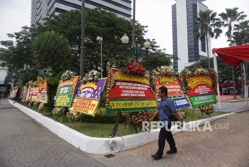 Warga melintas disamping karangan bunga yang berisi ucapan selamat kepada Anies Baswedan dan Sandiaga Uno di Balai Kota DKI Jakarta, Senin (16/10).